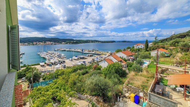 A marina with boats docked, a view of the sea, and surrounding greenery. - Apartments Sanja (Rab)