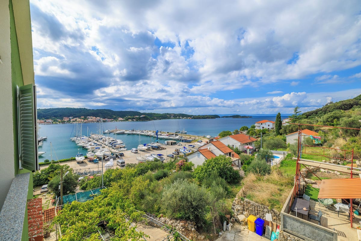 A marina with boats docked, a view of the sea, and surrounding greenery.