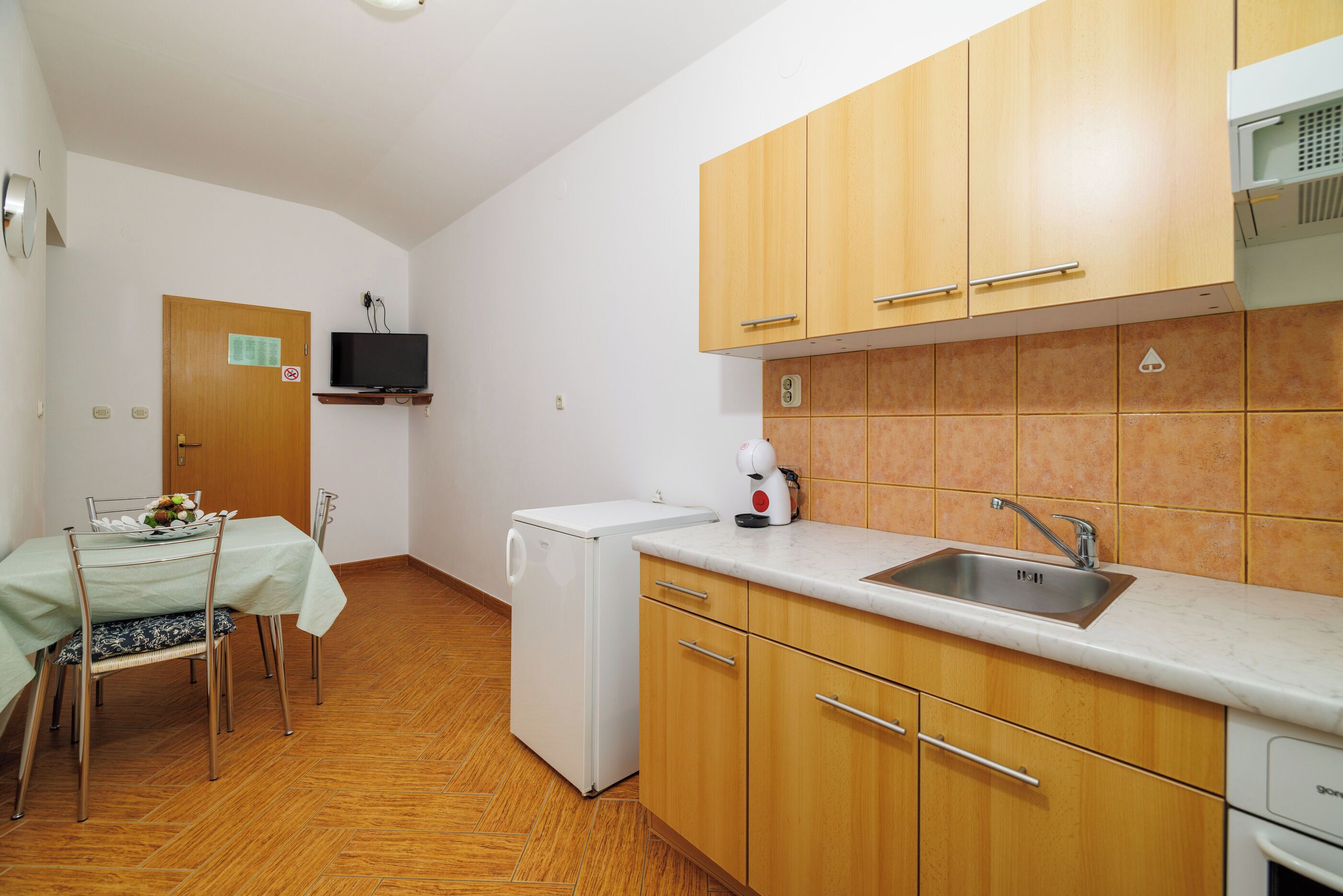 A compact kitchen with wooden cabinets, a built-in microwave, a sink, and a dining area with a table and chairs.