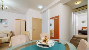 A modern living room with a glass-top table, a sofa, a chair, and a wooden door. - Apartments Sanja (Rab)