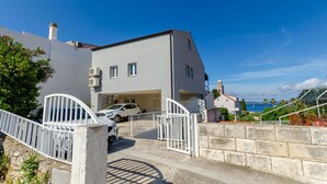 A two-story house with a garage, white exterior, and a view of the sea. - Apartments Marika (Hvar)