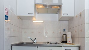 A compact kitchen with white cabinets, a stainless steel sink, and a built-in range hood. - Apartments Marika (Hvar)