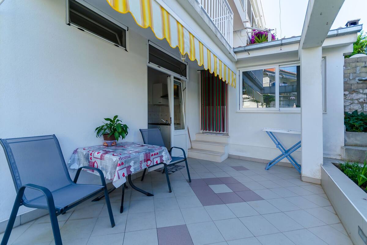 A patio area with a table and chairs, a potted plant, and a staircase leading to an upper level.