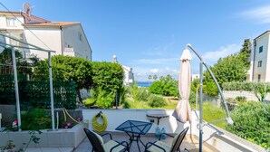 A patio with a table and chairs, a water hose, and a view of greenery and buildings. - Apartments Marika (Hvar)