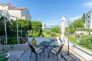 Eine Terrasse mit Tisch und Stühlen, einem Wasserschlauch und Blick auf Grünflächen und Gebäude.