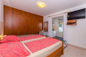 Ein Schlafzimmer mit zwei Betten, einem Holzschrank, einem Fernseher und einer kleinen Küchenzeile.