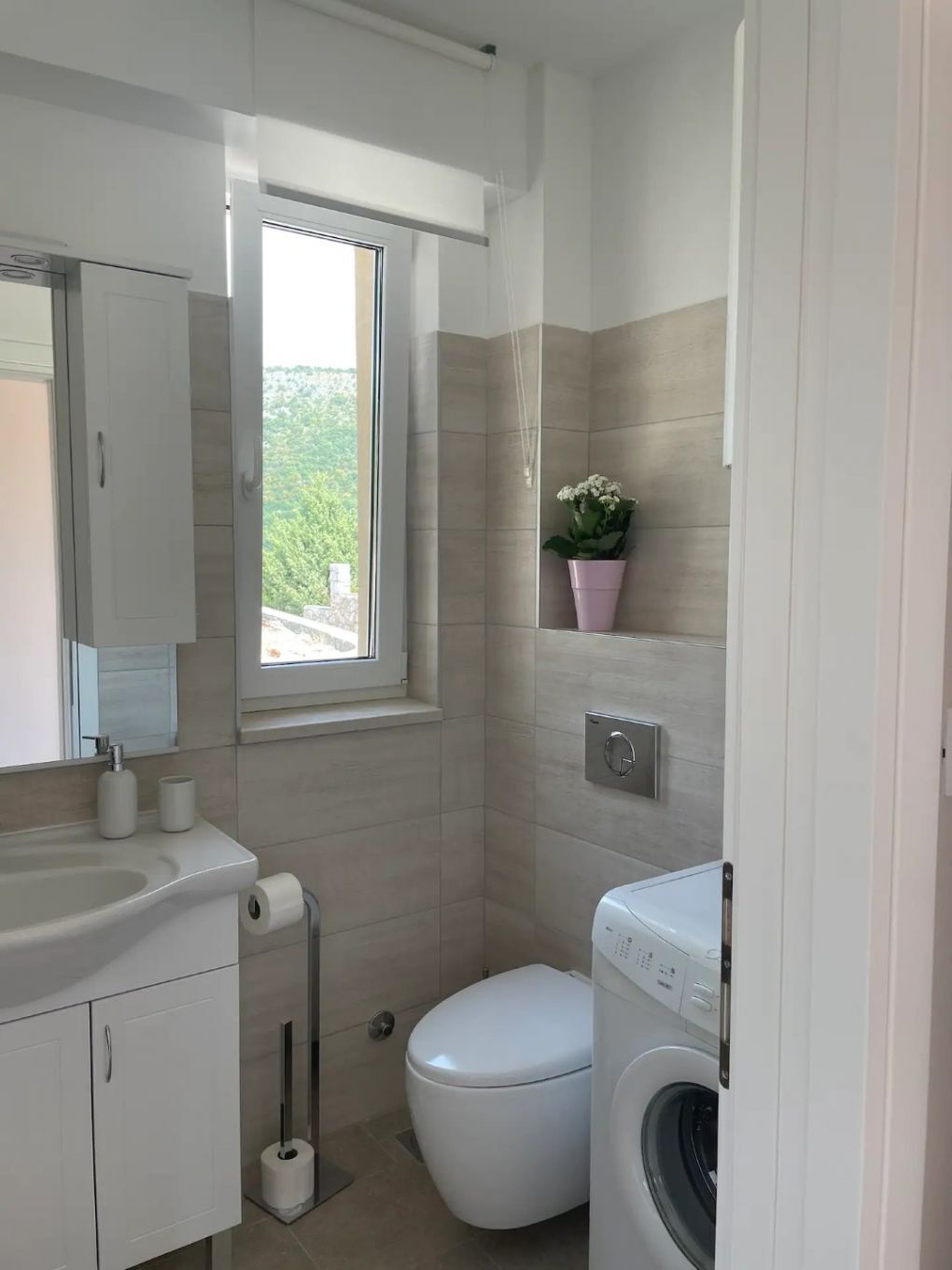 Et lille badeværelse med toilet, vaskemaskine og et vindue med naturligt lys.