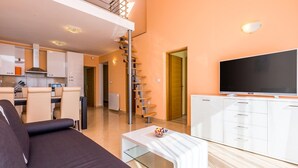 A modern living room with a sofa, a glass coffee table, a flat-screen TV, and a kitchen area with cabinets and a staircase. - Apartments Kostrena (Kostrena)