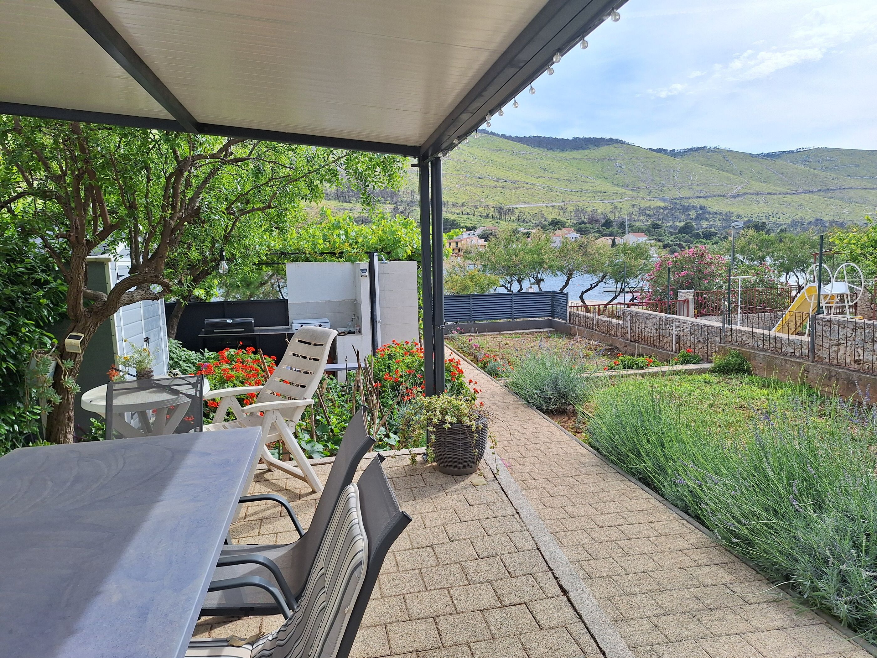 Une terrasse extérieure avec une table et des chaises, un barbecue et une vue sur un lac et des collines.