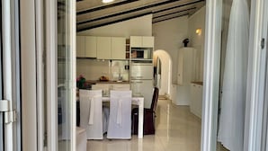 A modern kitchen with white cabinets, a dining table with chairs, and a refrigerator. - Apartments Neve Beachfront (Sibenik)
