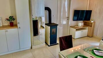 A compact living space with a kitchenette, a dining area with a table set for two, and a television mounted on the wall.