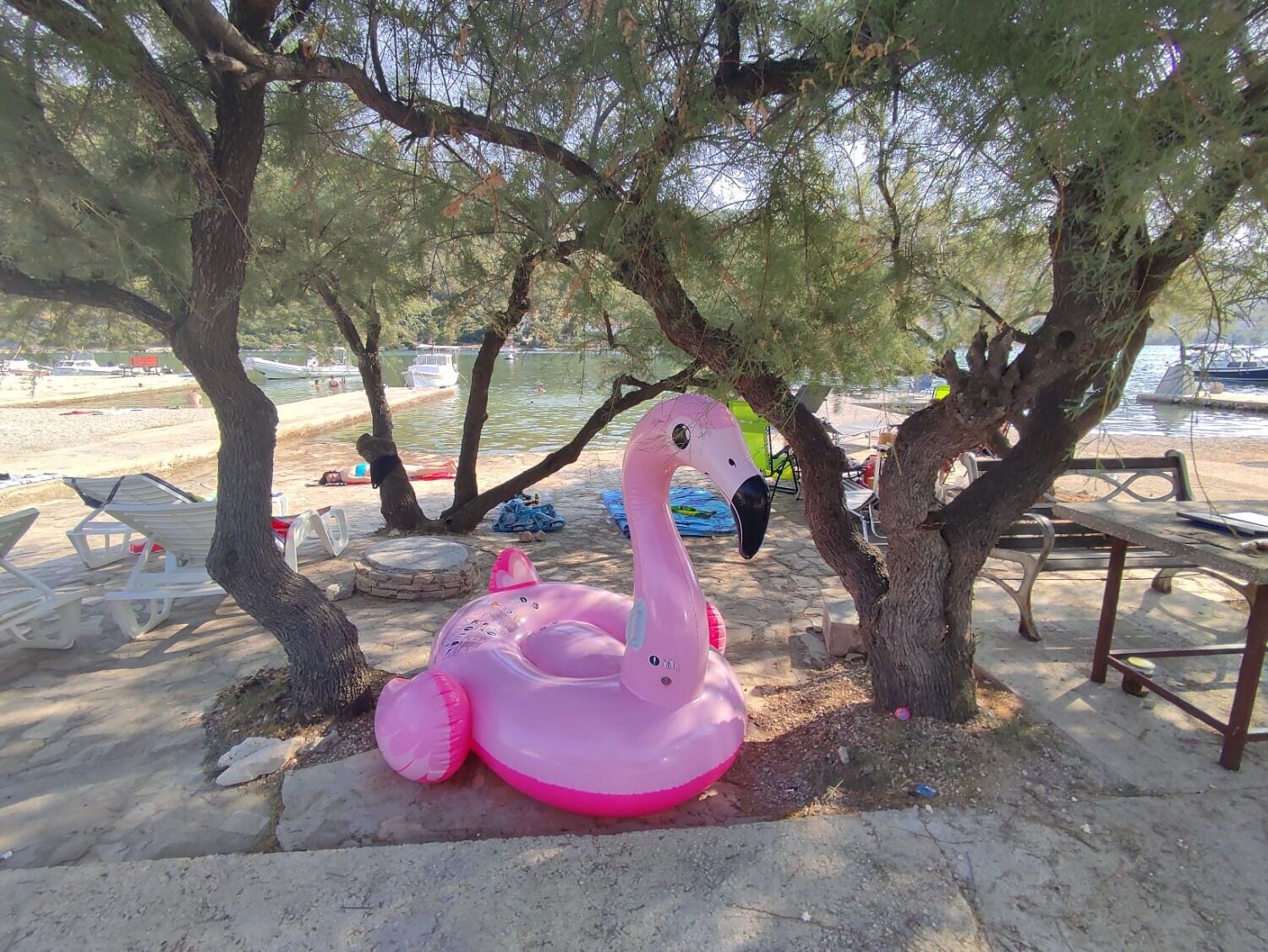 A beach scene with a pink inflatable flamingo, trees, and beach chairs.
