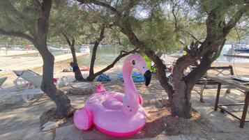 A beach scene with a pink inflatable flamingo, trees, and beach chairs.