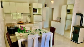 A modern kitchen with white cabinets, a dining table set for four, and a small refrigerator. - Apartments Neve Beachfront (Sibenik)