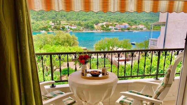 A balcony with a table and chairs, overlooking a scenic view of a lake and hills. - Apartments Neve Beachfront (Sibenik)