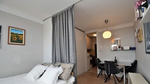 A modern bedroom with a bed, a desk, and a chair. There is a painting on the wall and a curtain covering a window. - Apartment City (Rijeka)