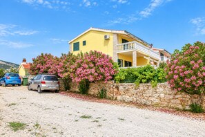 A yellow building with a stone wall, parked cars, and flowering bushes. - Apartments Josipa (Primosten)