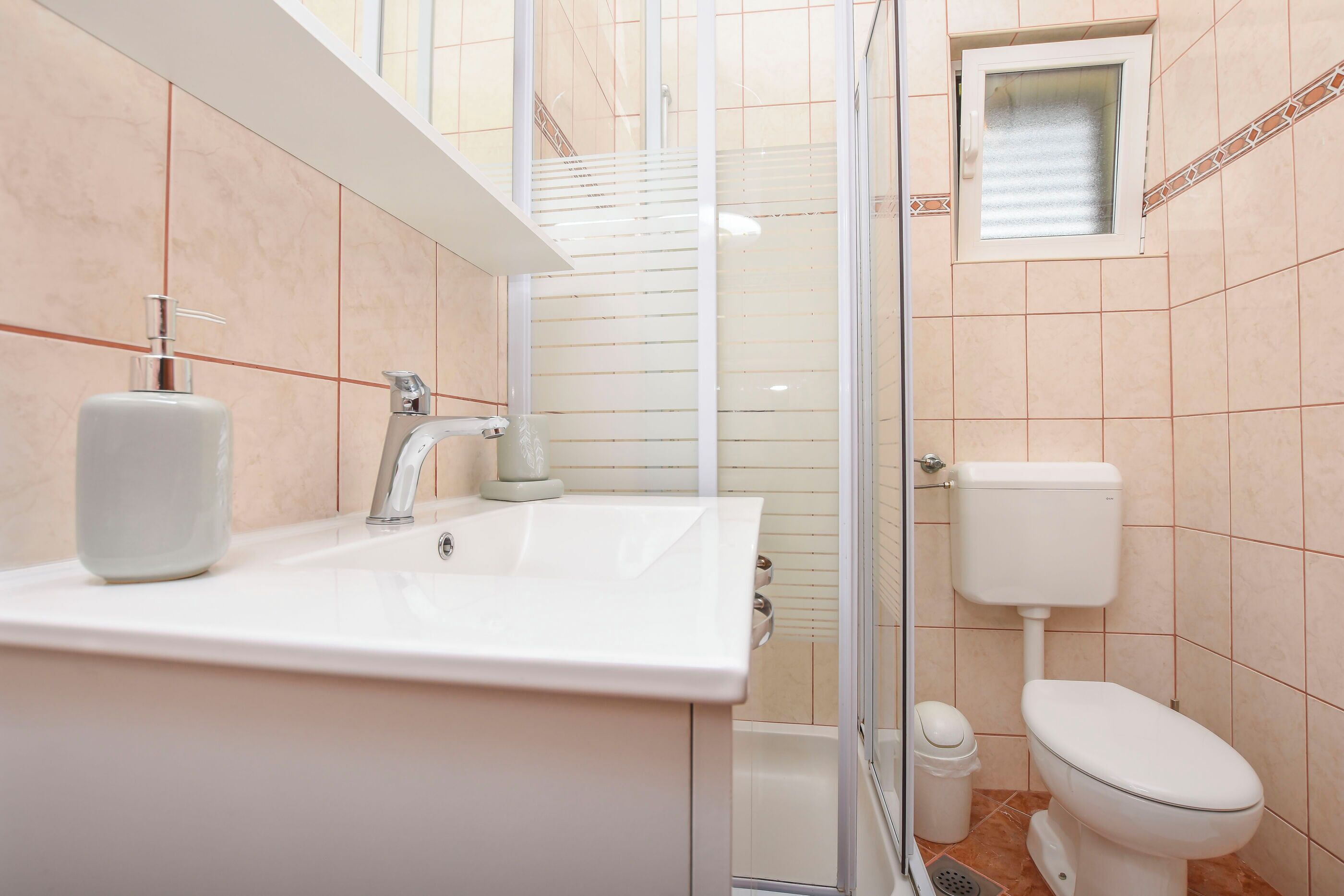 Une salle de bain avec un lavabo blanc, un miroir, des toilettes et un espace douche.