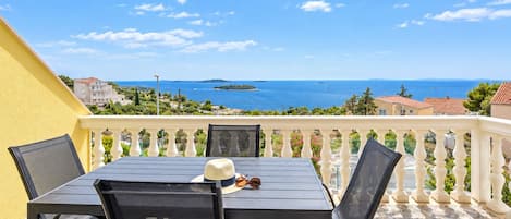 A balcony with a table and chairs, overlooking a coastal view with houses and the sea.
