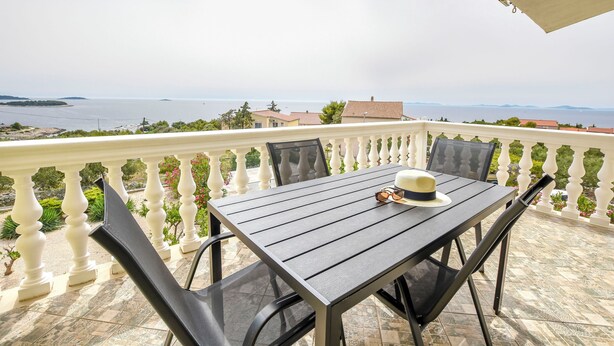 Un balcone con tavolo e sedie, affacciato su una vista costiera.