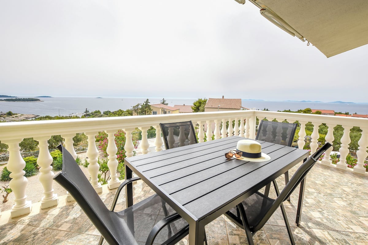 A balcony with a table and chairs, overlooking a coastal view.