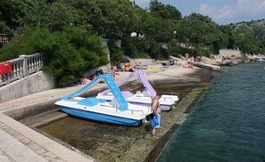 A waterfront area with boats docked, a stone wall, and people in swimwear. - Apartment Rose (Vinodol)