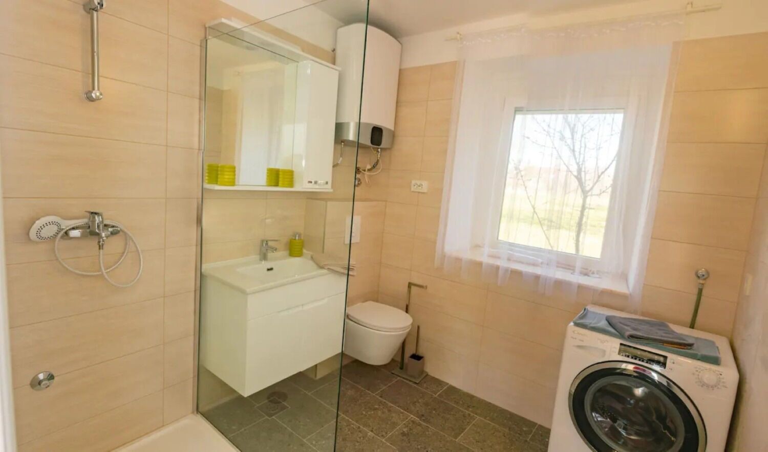 A compact bathroom with a shower, sink, toilet, and a washing machine.