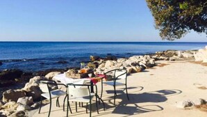 A beachside table with chairs and a tablecloth, set against a backdrop of the sea and a clear sky. - Apartment Mirella (Umag)