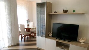 A modern living room with a flat-screen TV, a coffee table, and a dining area with chairs and a table. - Apartment Mirella (Umag)