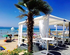 A beachside area with a palm tree, white umbrellas, and lounge chairs under a white canopy. - Apartment Mirella (Umag)