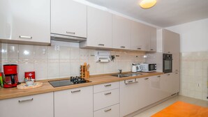 Eine moderne Küche mit weißen Schränken, einer Holzausziehtafel, einer Kaffeemaschine, einer Mikrowelle und einem Wasserkocher.