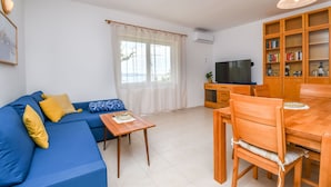 Ein Wohnzimmer mit blauem Sofa, Esstisch aus Holz und einem Fernseher auf einem Schrank.