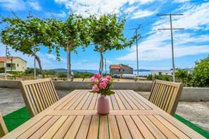 A wooden table with a pink vase of flowers, two wooden chairs, and a view of houses and trees in the background. - Apartment Live (Seget)