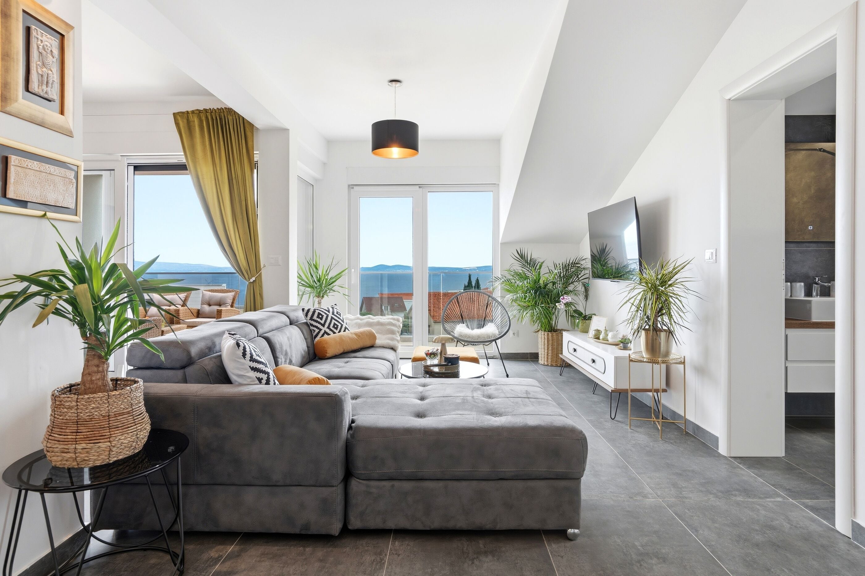 A modern living room with a grey sectional sofa, a round coffee table, and a large window with a view of the sea.