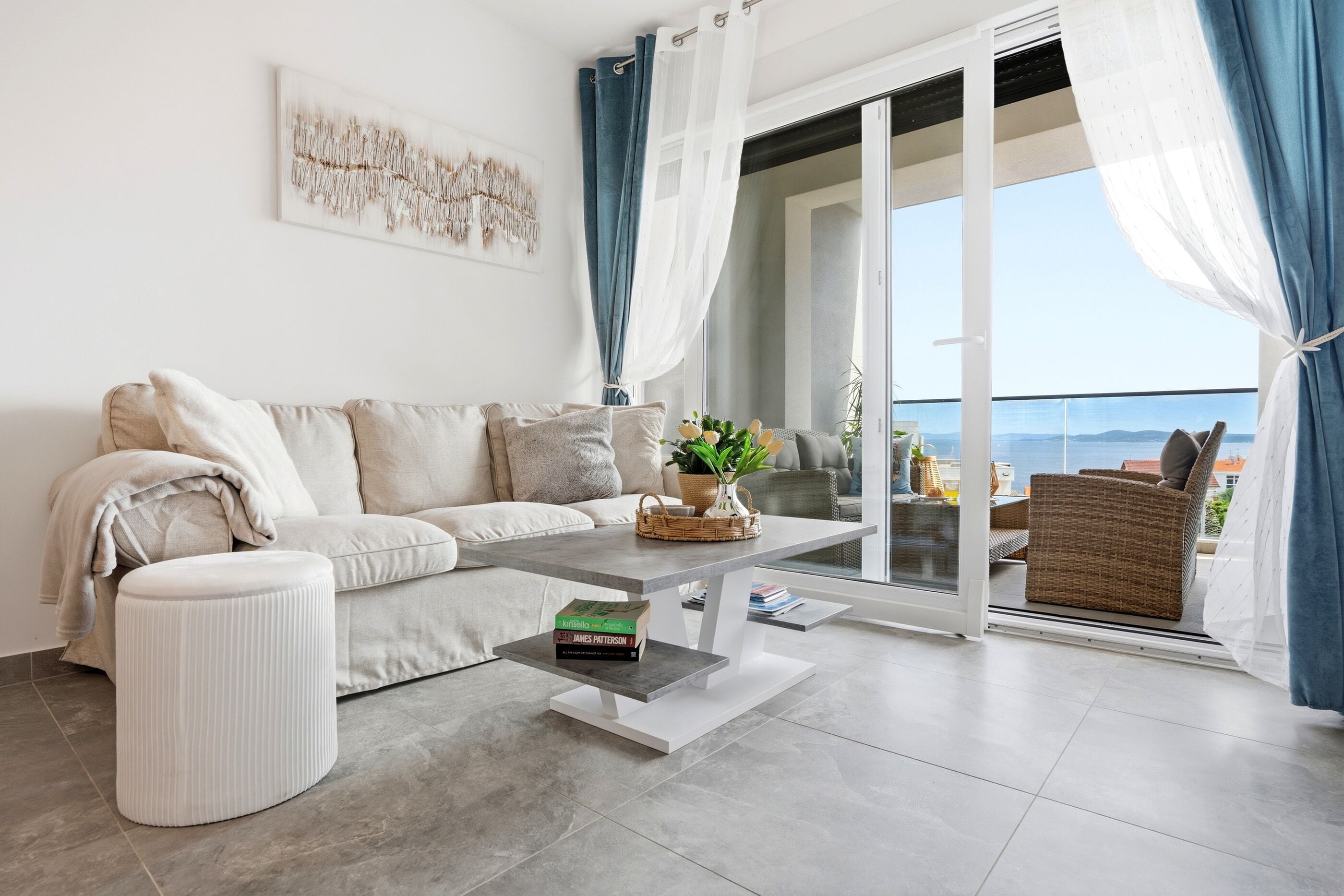 A modern living room with a sofa, a coffee table, and a view of the sea through a glass door.