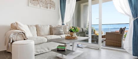 A modern living room with a sofa, a coffee table, and a view of the sea through a glass door.