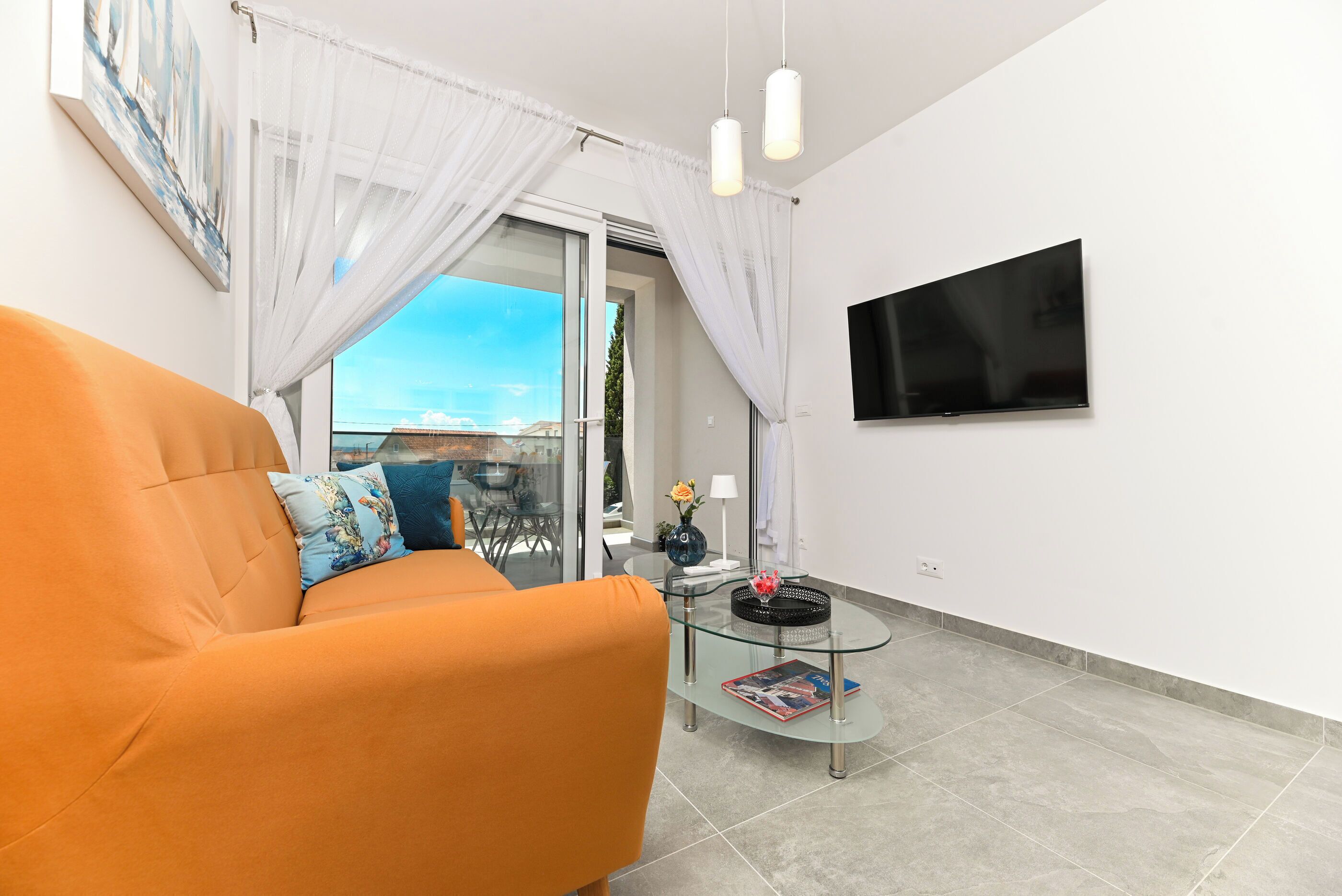Una sala de estar moderna con un sofá, una mesa de centro de vidrio, un televisor de pantalla plana y vistas a través de una puerta de cristal.