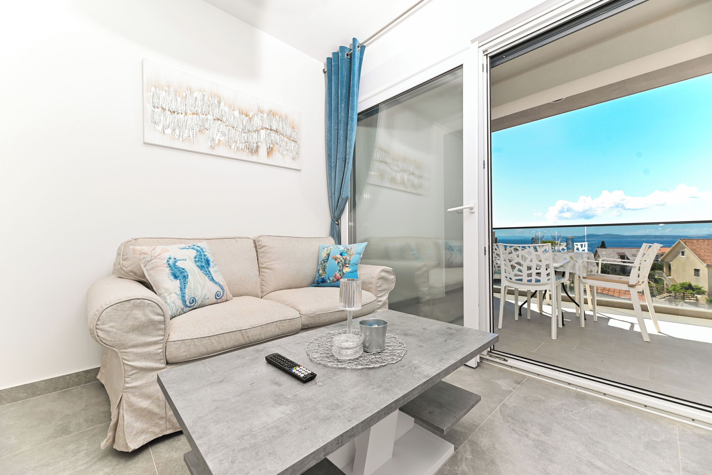 A modern living room with a sofa, a coffee table, and a glass door leading to an outdoor seating area.