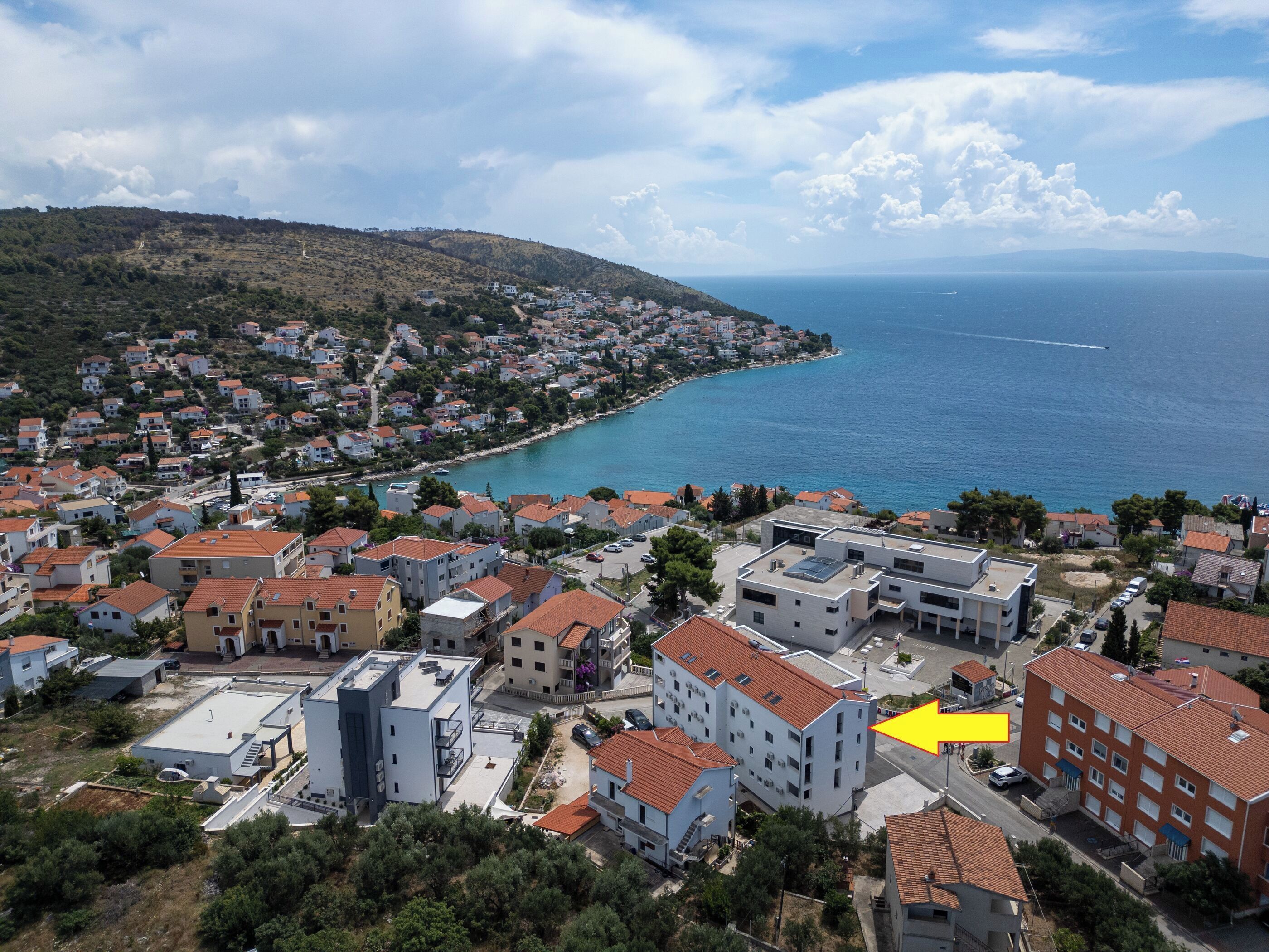 A coastal town with a mix of residential buildings, some with red-tiled roofs, and a view of the sea.