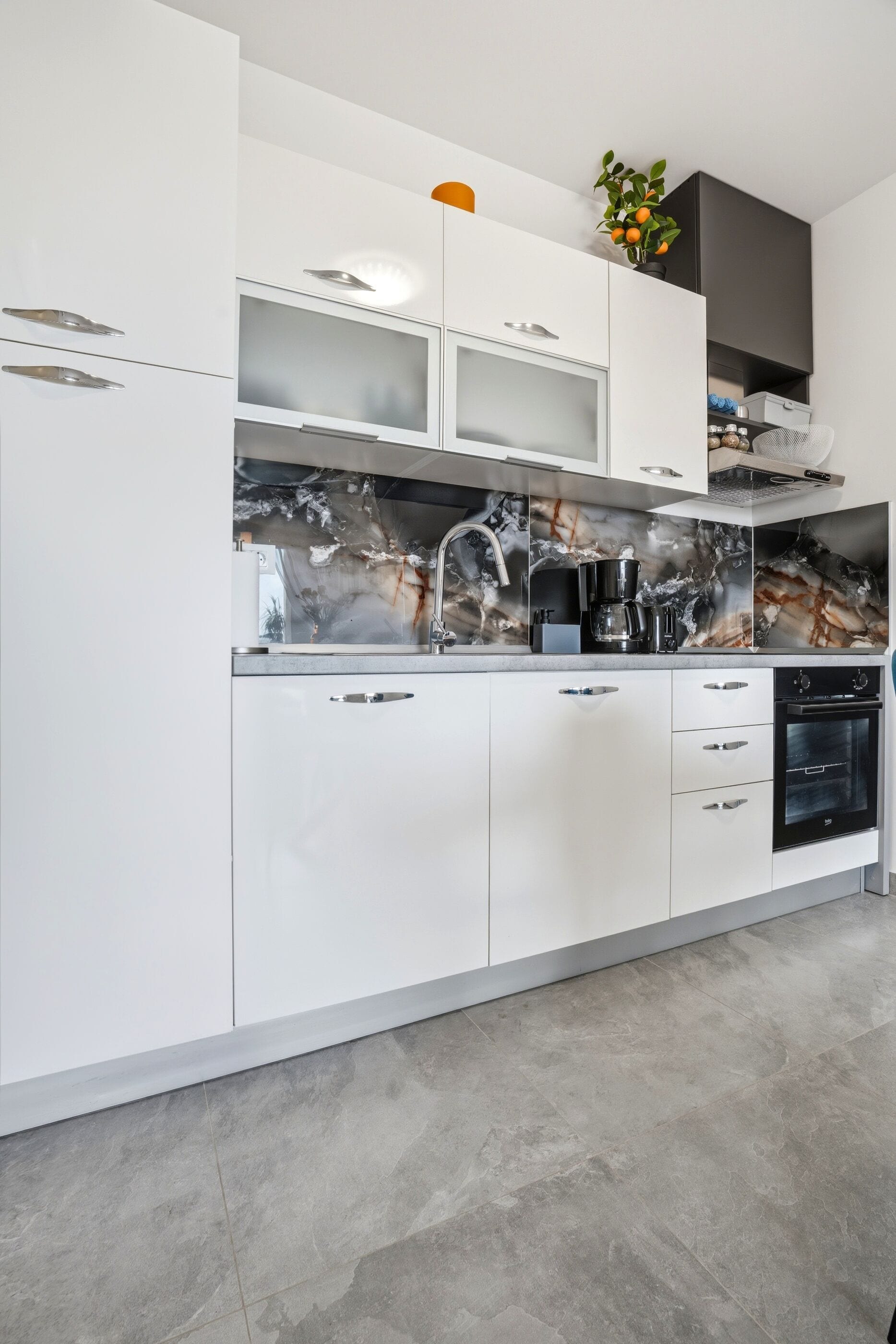 A modern kitchen with white cabinetry, a marble backsplash, and a built-in oven.