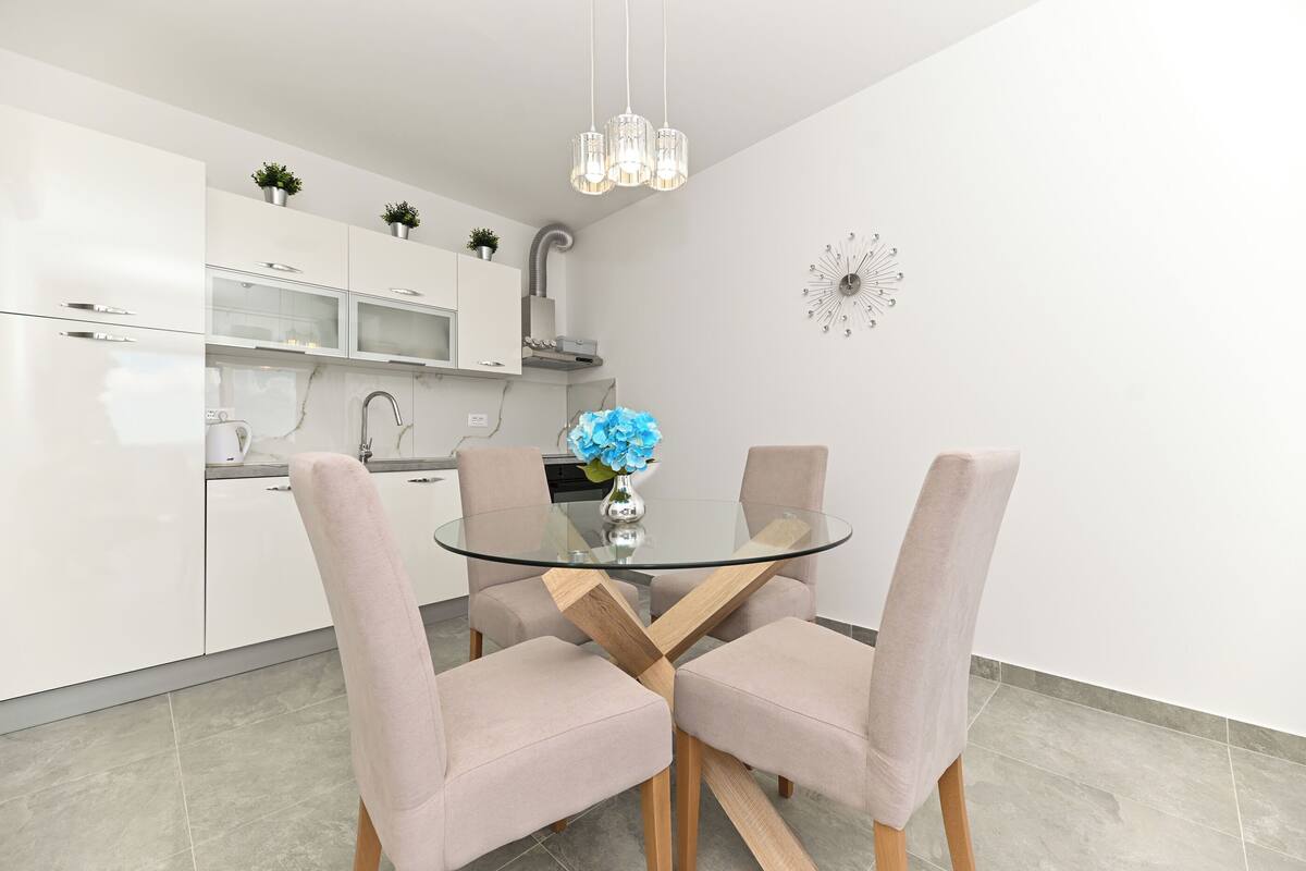 A modern kitchen with white cabinets, a glass dining table, and four chairs.
