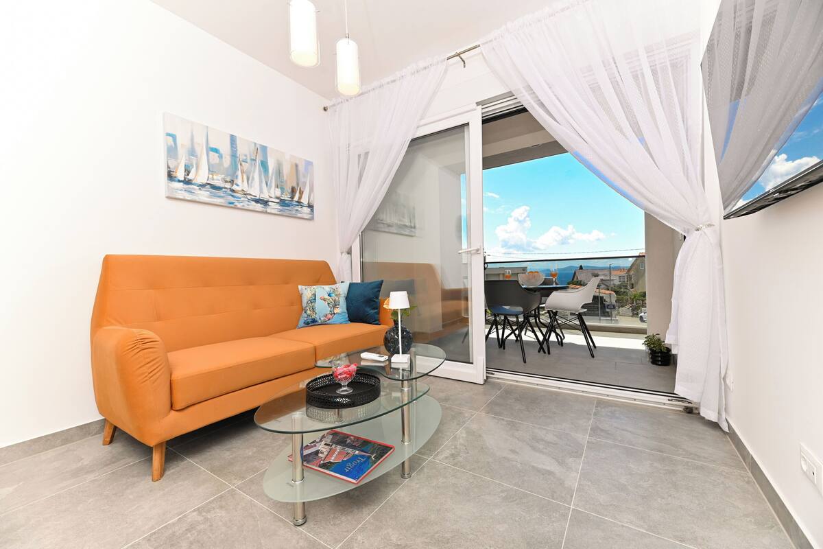 A modern living room with a glass coffee table, orange sofa, and a painting on the wall.
