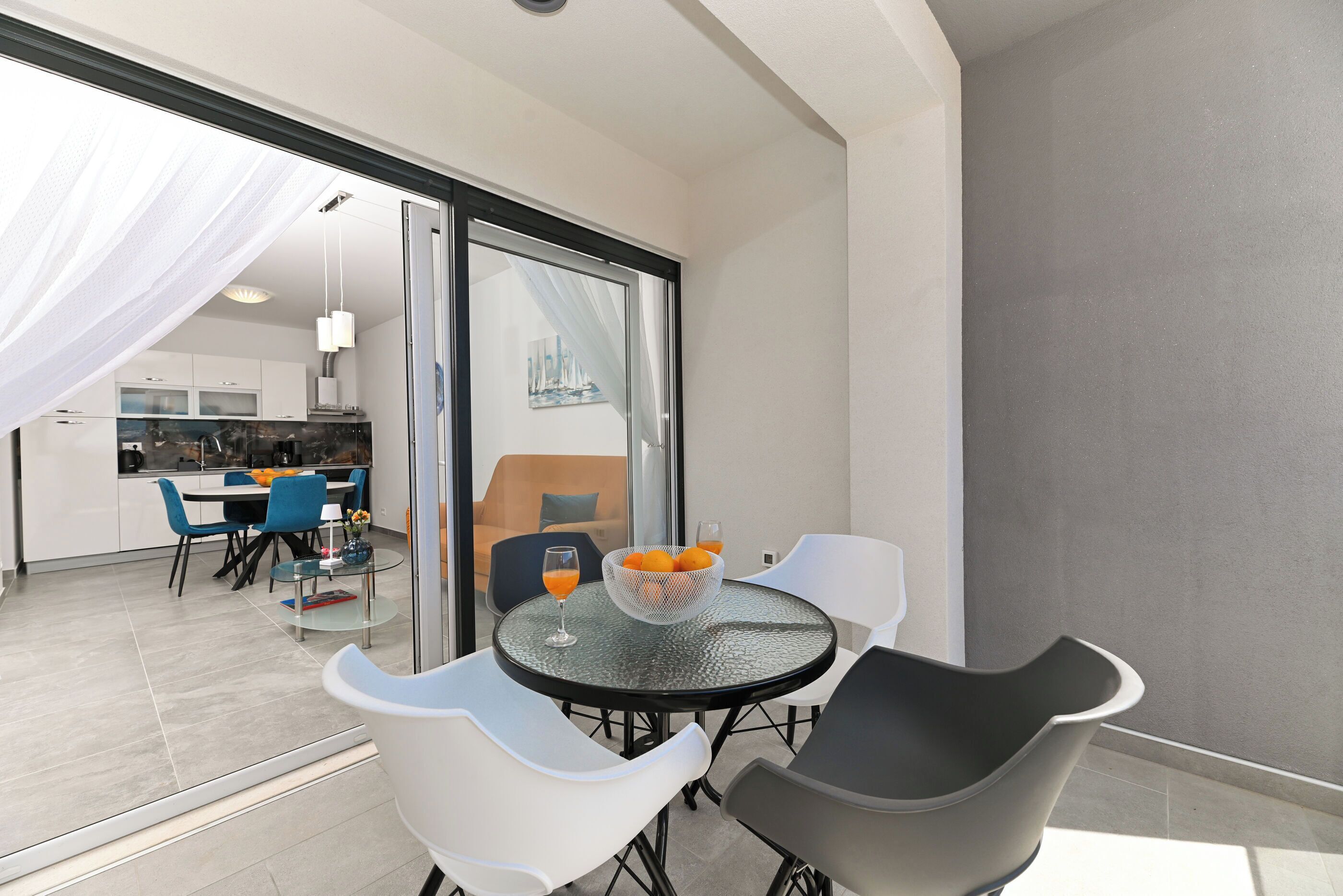 A modern dining area with a glass table, white and black chairs, and a bowl of oranges.