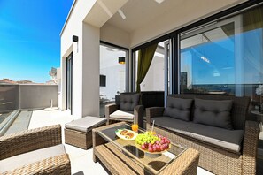 A balcony with wicker furniture, a glass table with fruit and a drink, and a sofa with cushions. - Apartments Diva (Okrug)