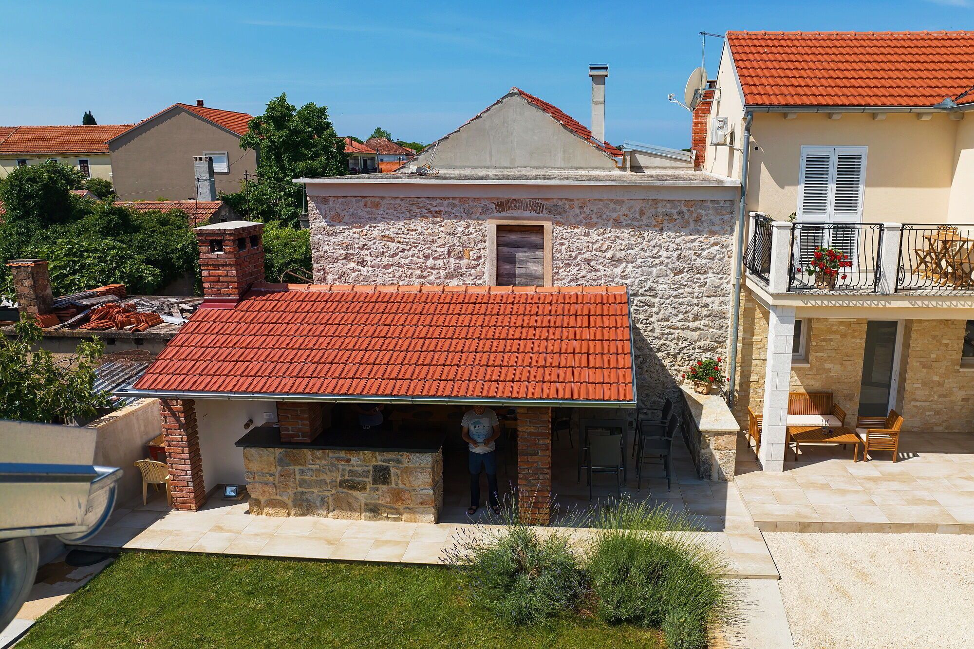 A stone house with a red-tiled roof, a small balcony with outdoor seating, and a stone chimney.