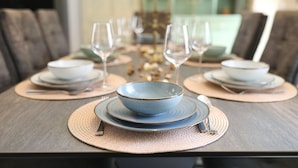 A dining table set with plates, bowls, and wine glasses, with a woven placemat underneath each set. - House Bona (Sukosan)