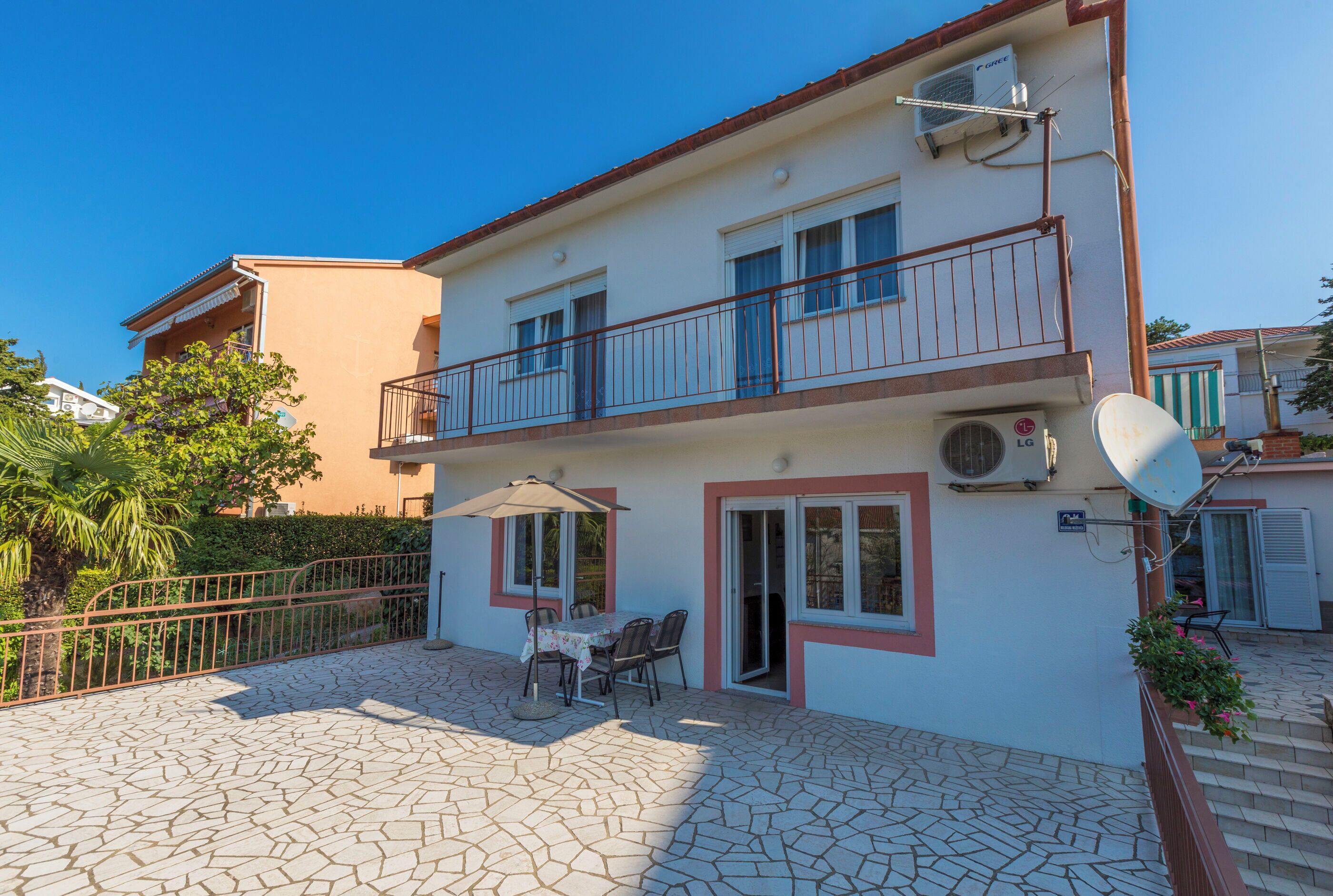A two-story building with a balcony, a patio with a table and chairs, and a satellite dish.