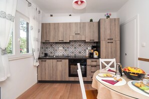 A modern kitchen with wooden cabinets, a patterned backsplash, and a dining area with a table set for breakfast. - House Mirna (Rogoznica)