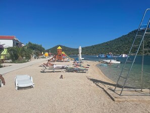 A beach with sun loungers, a children's play structure, and boats in the water. - House Mirna (Rogoznica)
