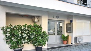 A building entrance with a glass door, a small balcony, and potted plants. - Apartment Leo (Ploce)
